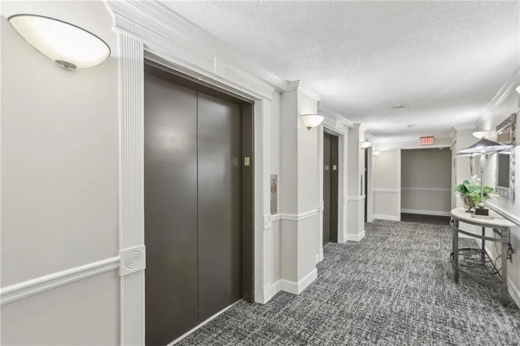Corridor featuring ornamental molding, a textured ceiling, and dark colored carpet