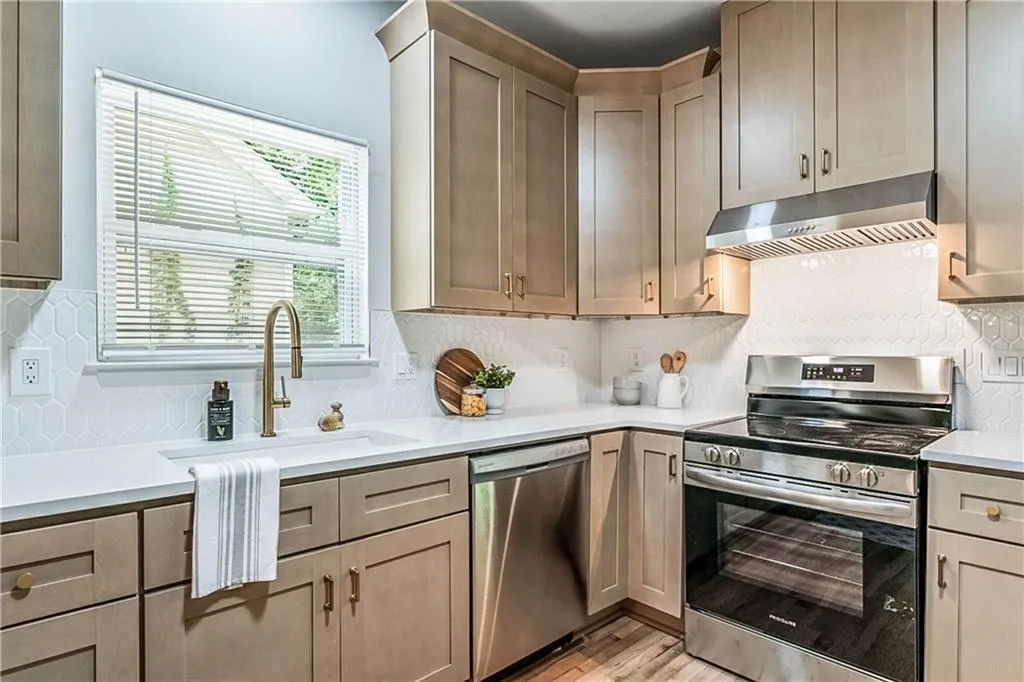 Kitchen with appliances with stainless steel finishes, under cabinet range hood, backsplash, and light wood-style flooring