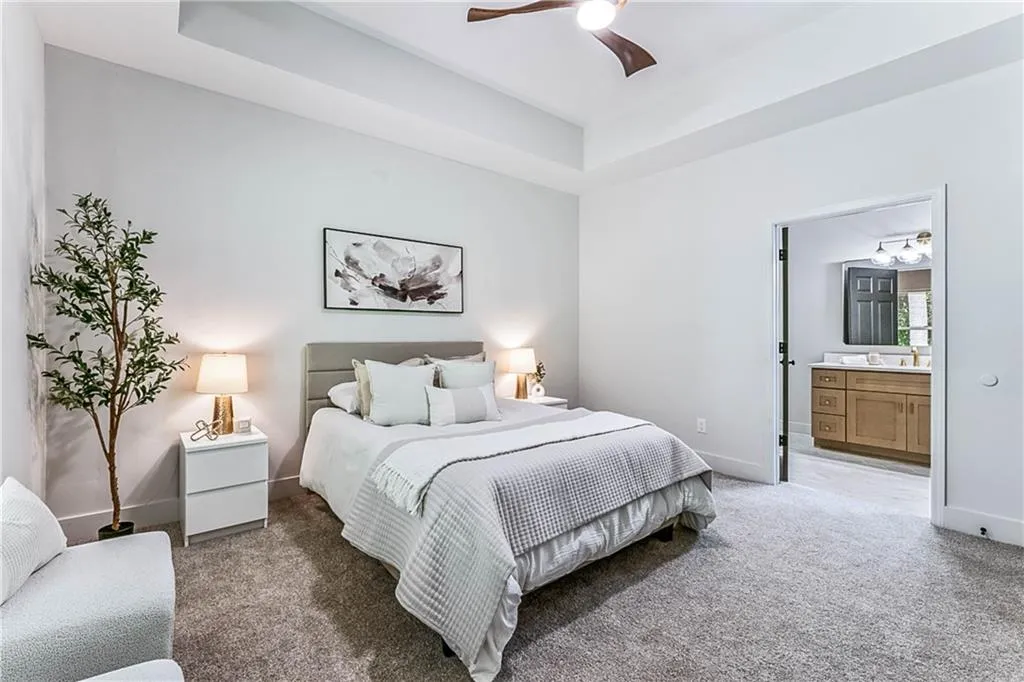 Bedroom with carpet, a raised ceiling, ensuite bath, and a ceiling fan