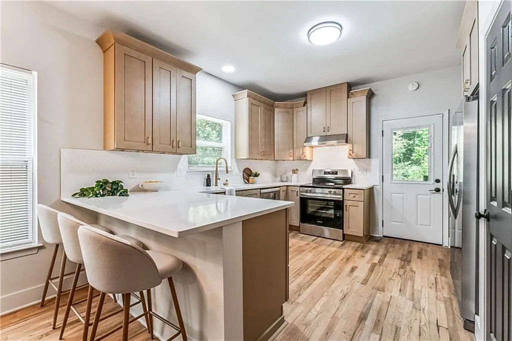 Kitchen with a peninsula, a kitchen breakfast bar, appliances with stainless steel finishes, light wood-type flooring, and light stone counters