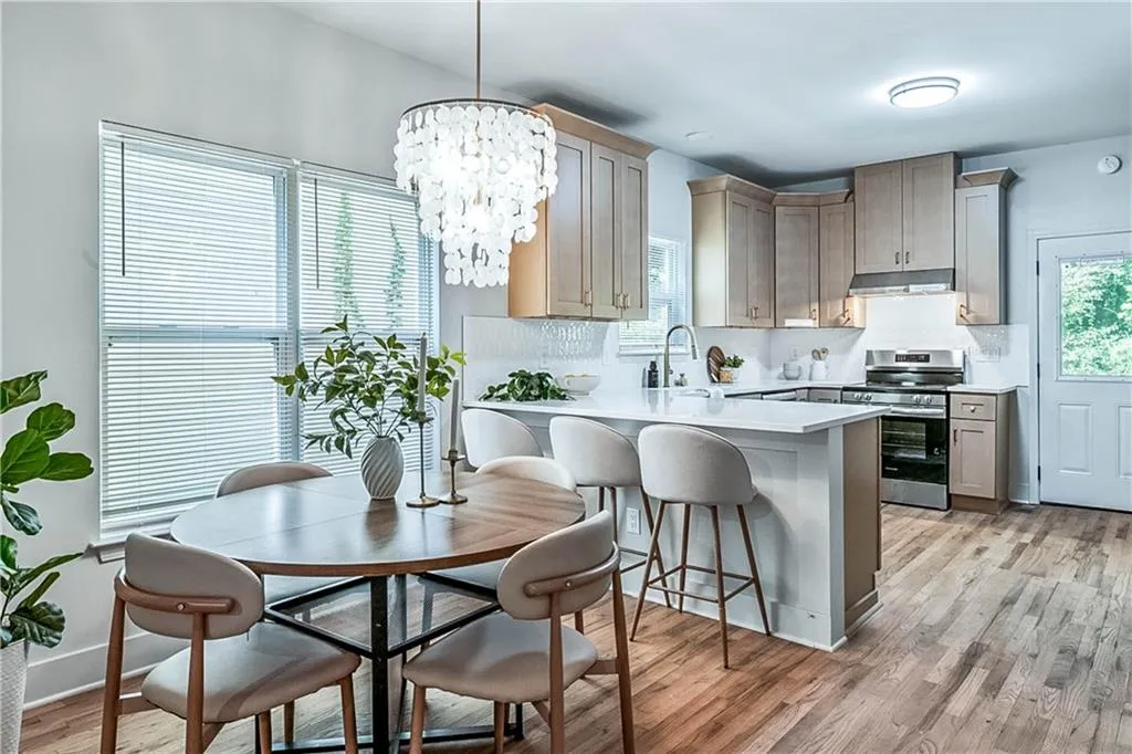 Kitchen with electric stove, light wood-style floors, tasteful backsplash, decorative light fixtures, and a breakfast bar