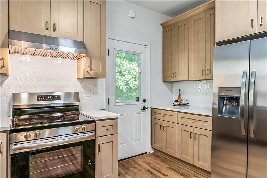 Kitchen featuring stainless steel appliances, under cabinet range hood, light wood-style floors, decorative backsplash, and light brown cabinets