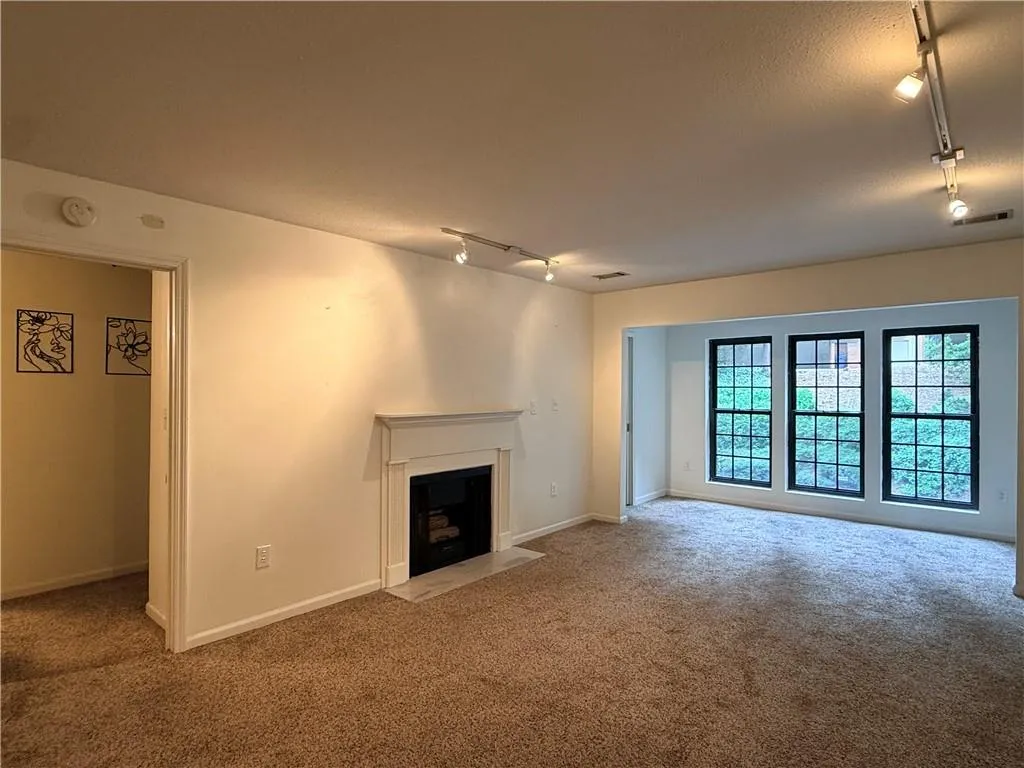 Carpeted living area featuring a fireplace with a classic mantel, track lighting, and a trio of windows with dark frames