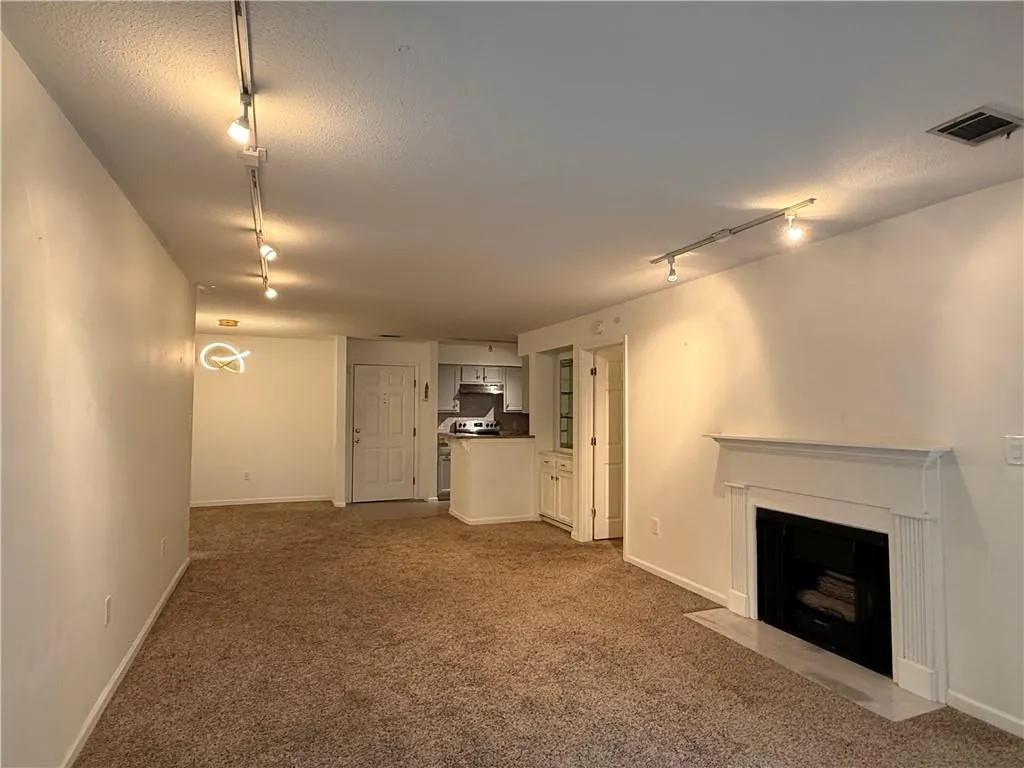 Carpeted living area featuring a fireplace with a white mantel, track lighting, and built-in cabinetry