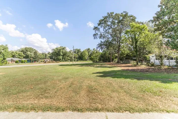 Expansive lot featuring a large grassy area, mature trees, and a concrete pathway