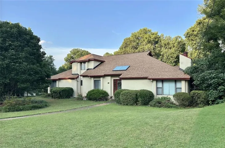 Stucco exterior with a brown shingle roof, integrated solar panel, and mature landscaping