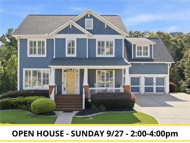 7327 Rocking Chair Lane in the Reunion golf community in Hoschton, GA. Two-story Craftsman-style home with blue siding, stone accents, a covered front porch, and a landscaped front yard.
