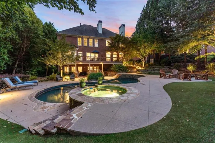 Brick exterior with multiple windows, multi-level deck, concrete patio surrounding a swimming pool with an attached spa, and a landscaped yard