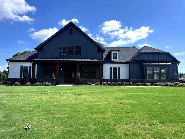 Board and batten siding with white accents, covered front porch with substantial pillars, dark-framed windows, gabled roofline, and landscaped foundation planting