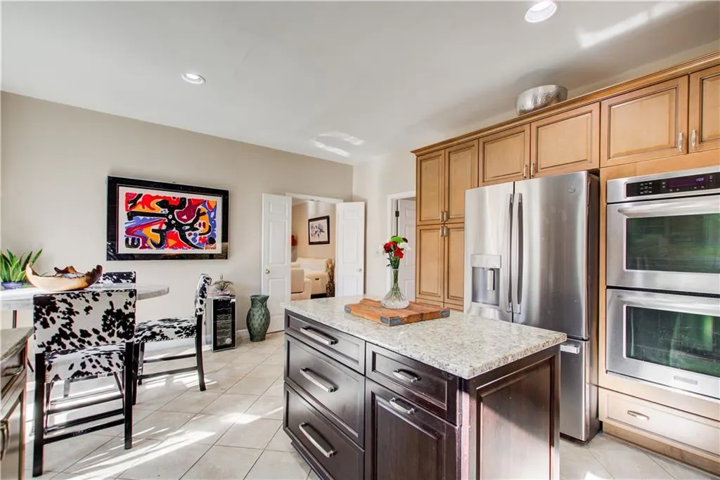 Kitchen with appliances with stainless steel finishes, light tile patterned flooring, recessed lighting, light stone countertops, and dark brown cabinets