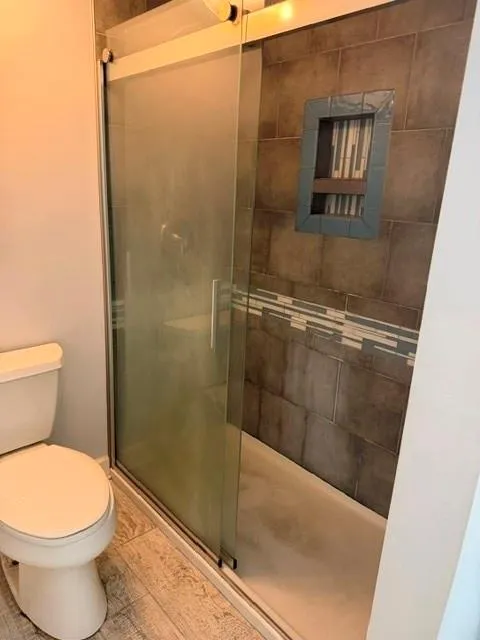 Enclosed shower with sliding frosted glass door, tiled shower surround, recessed shower niche, and wood-finish flooring