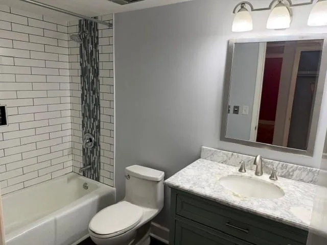 Bathtub with subway tile surround and mosaic accent, vanity with stone countertop and integrated sink, framed mirror, and brushed nickel fixtures