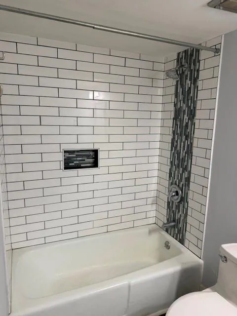 Bathtub with white subway tile surround, decorative mosaic tile accent, built-in shower niche, and polished chrome fixtures