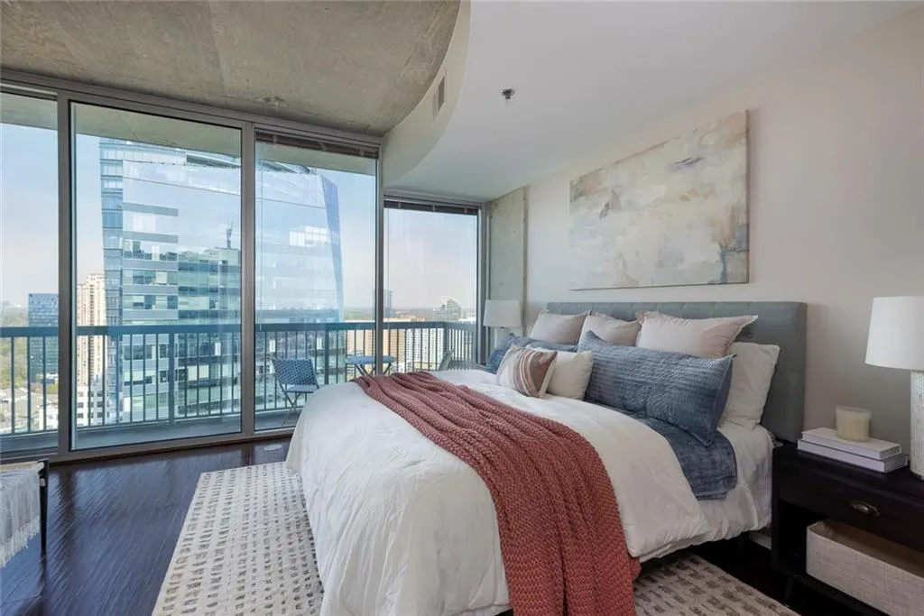 Bedroom featuring wood finished floors, a city view, expansive windows, and access to outside balcony.