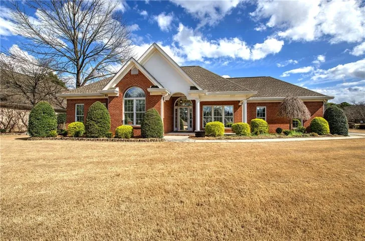 View of front of property with brick siding, a front yard, and roof with shingles