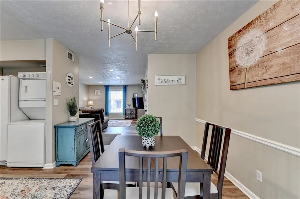 Dining space with stacked washer and clothes dryer, wood finished floors, a textured ceiling, a chandelier, and baseboards