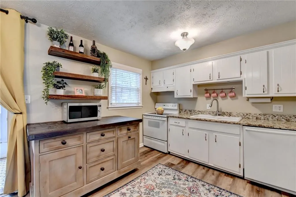 Kitchen with white appliances, a sink, light wood finished floors, open shelves, and a textured ceiling