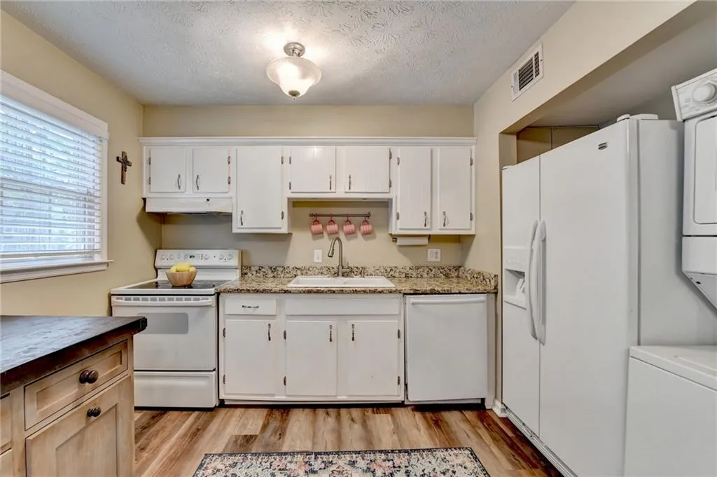 Kitchen with white appliances, a sink, light wood finished floors, white cabinets, and a textured ceiling