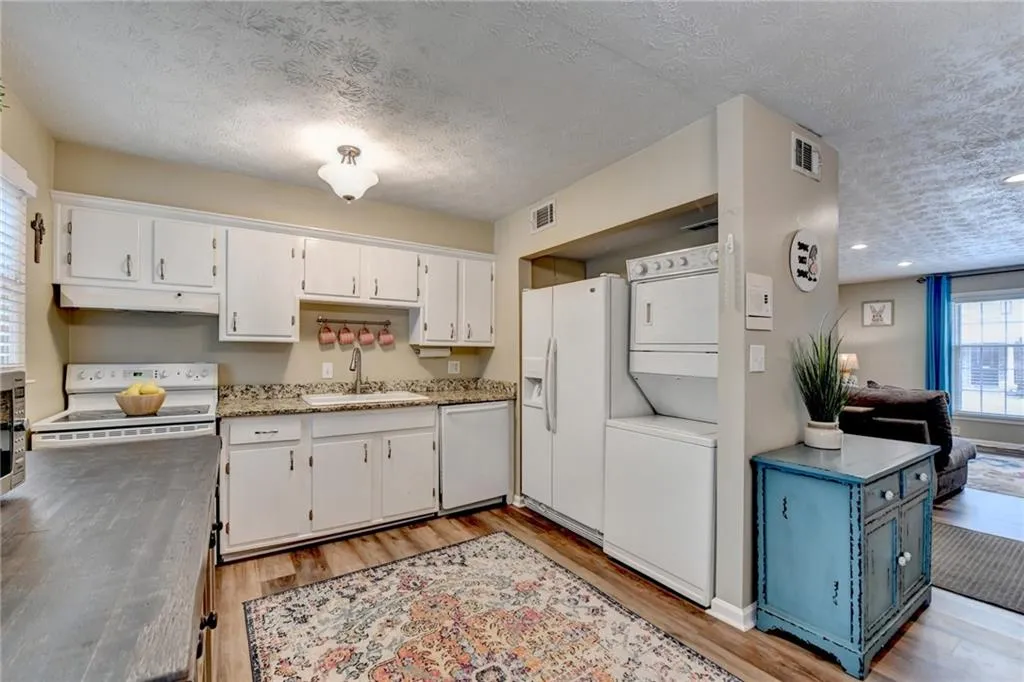 Kitchen with a sink, white appliances, stacked washer and clothes dryer, a textured ceiling, and under cabinet range hood