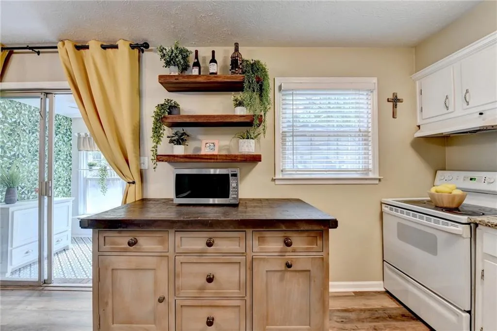 Kitchen featuring white range with electric cooktop, stainless steel microwave, under cabinet range hood, light wood-style flooring, and dark countertops