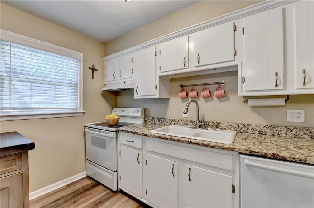 Kitchen with white appliances, a sink, under cabinet range hood, light wood-style flooring, and white cabinets