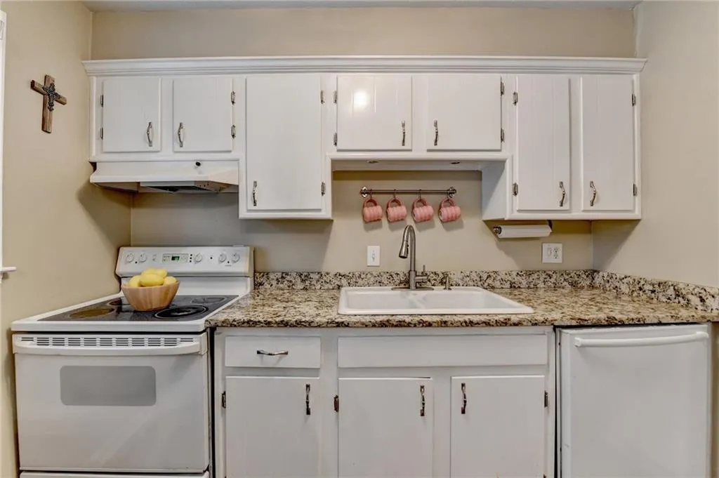 Kitchen with white appliances, a sink, under cabinet range hood, and white cabinets