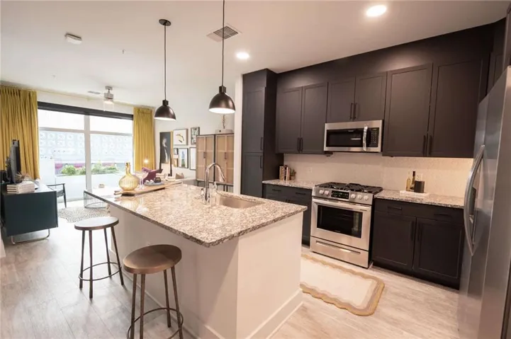 Kitchen featuring appliances with stainless steel finishes, a kitchen island with sink, a kitchen bar, sink, and light stone counters