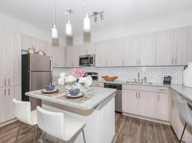 Kitchen featuring a breakfast bar area, hanging light fixtures, a kitchen island, light stone countertops, and appliances with stainless steel finishes