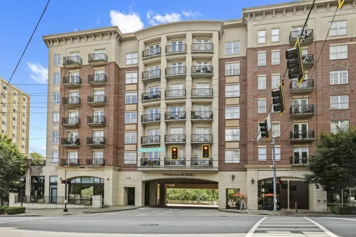 Multi-story building featuring brick and stone facade, private balconies, an arched drive-through entry, and ground-level retail spaces