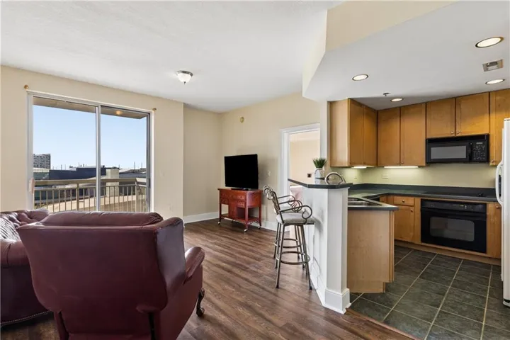 Open-concept living space featuring wood-finish flooring, a kitchen with wood cabinetry, a built-in microwave, and a window for natural light