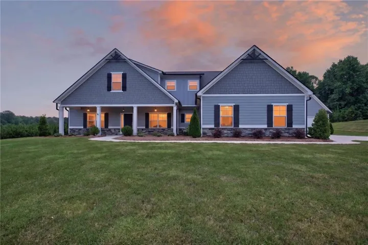 Expansive residential exterior featuring a light blue siding facade with dark grey shake accents, a covered front porch with white columns, and stone veneer skirting