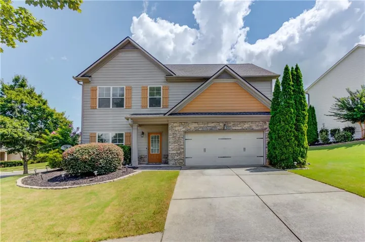 Siding exterior with stone accents, covered entry, attached garage, and landscaped front yard with mature plantings
