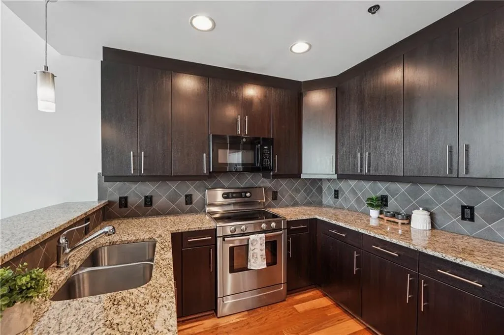 Kitchen with electric range, black microwave, a sink, light stone counters, and decorative backsplash