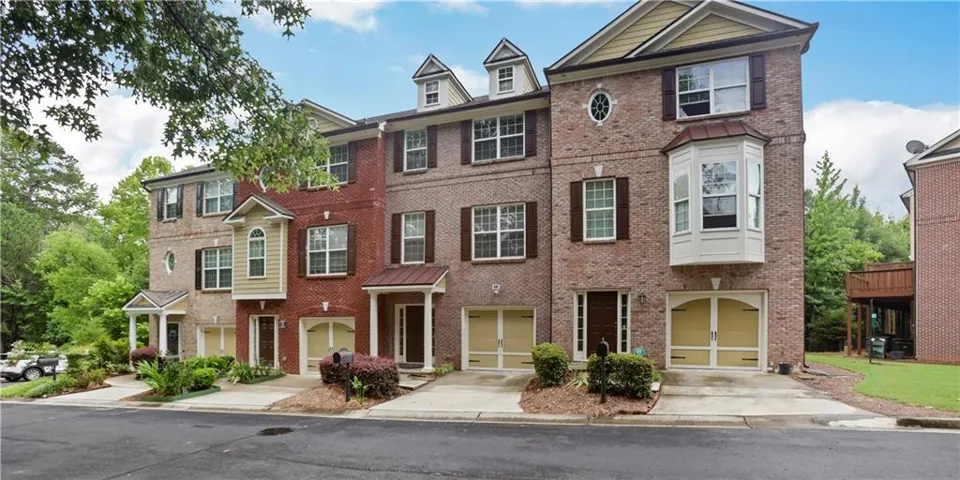 Brick facade townhome featuring multiple stories, shuttered windows, a bay window, and a ground-level garage