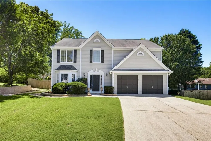 Two-story residence featuring light gray siding with white trim, a two-car attached garage, and a bay window