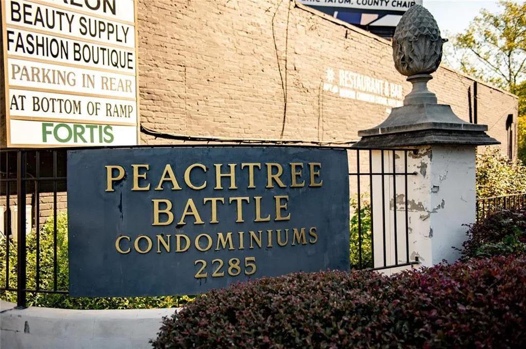 Peachtree Battle Condominiums signage featuring metal lettering on a dark rectangular plaque, set against a black metal fence with stone pier and decorative finial