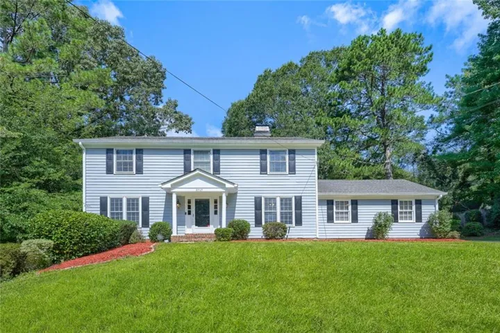 Two-story residence featuring light blue siding with dark shutters, a covered entry porch, and an expansive front lawn