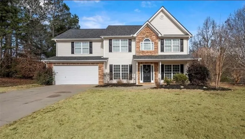Two-story residence featuring a gabled roof, stone façade accents, a covered front porch, and an attached two-car garage