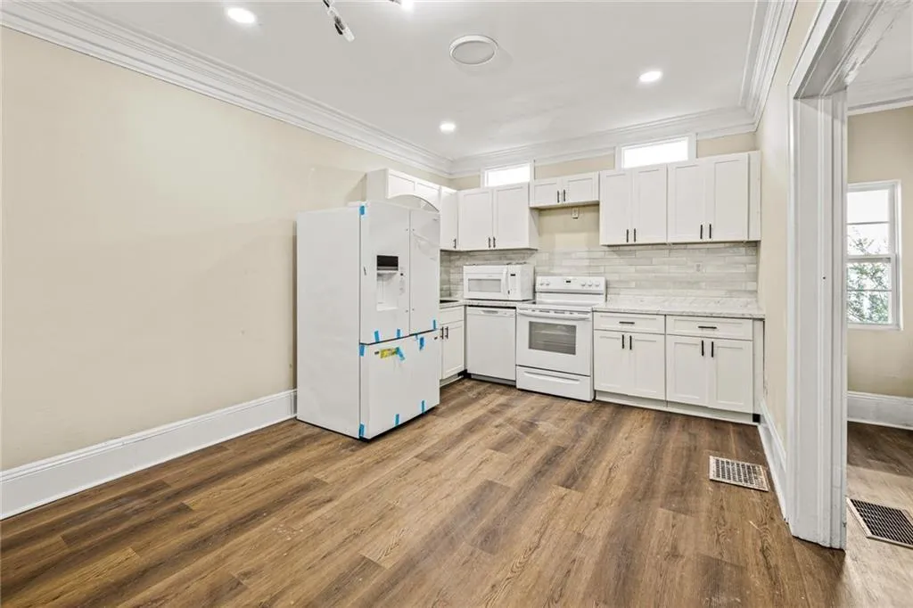 Kitchen featuring white appliances, white cabinetry, decorative backsplash, ornamental molding, and light countertops