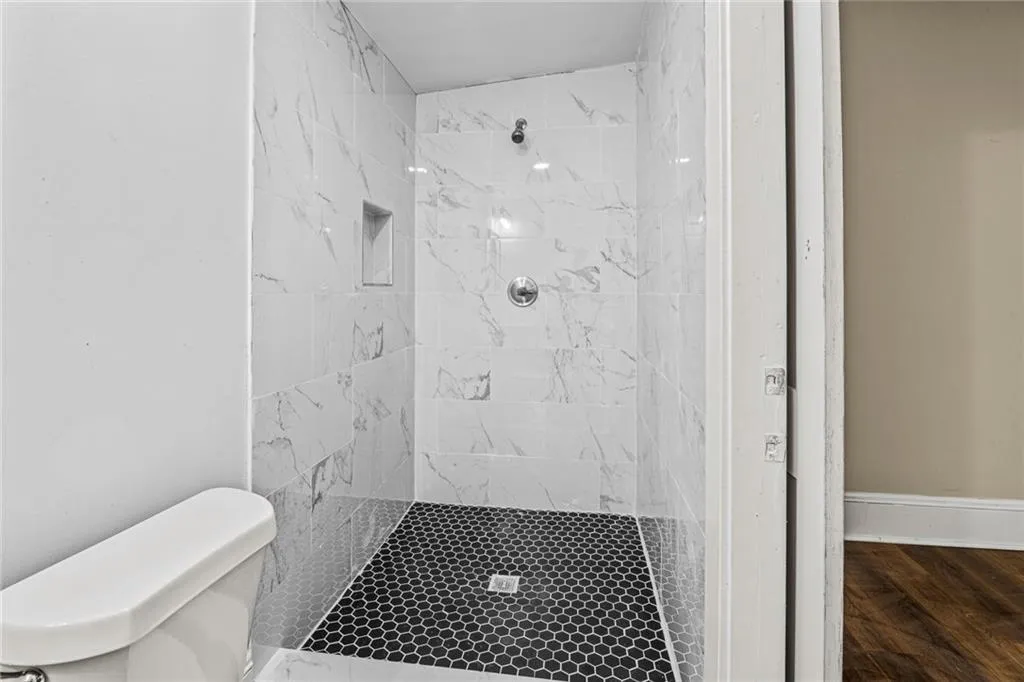 Full bathroom with a marble finish shower and dark wood-style floors
