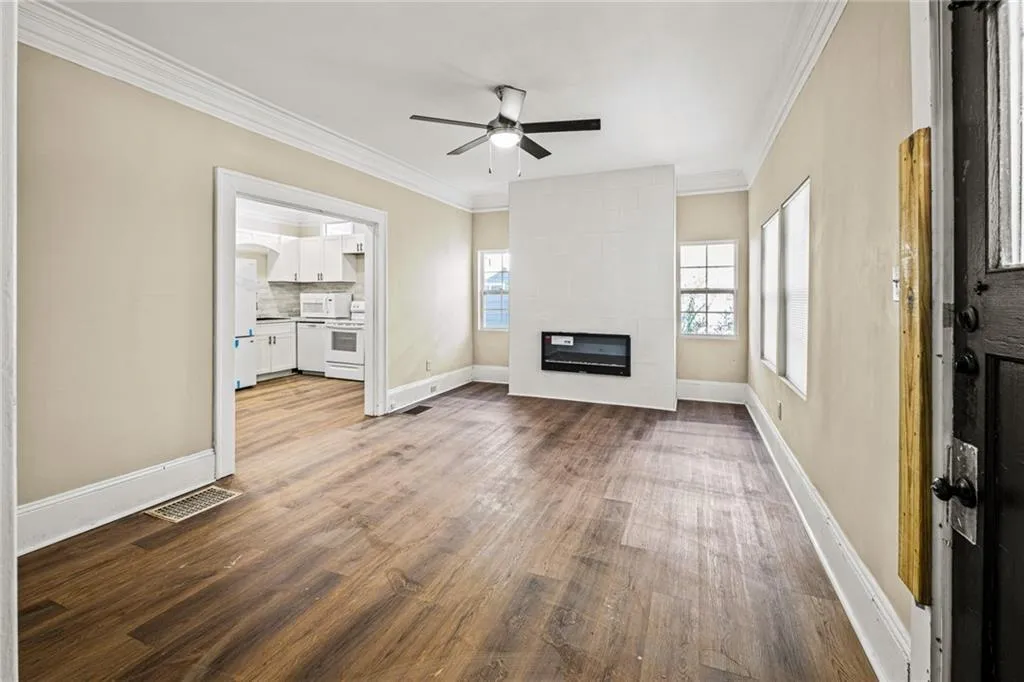 Unfurnished living room with crown molding, a fireplace, wood finished floors, and a ceiling fan