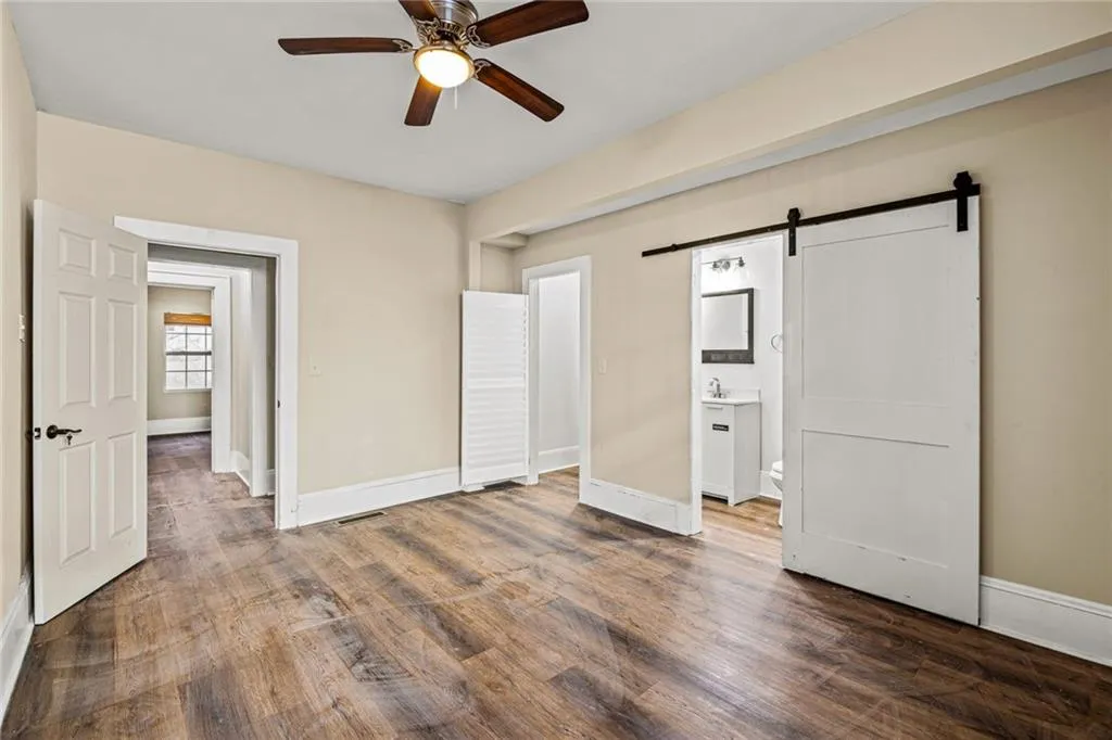 Unfurnished bedroom featuring a barn door, wood finished floors, ceiling fan, and ensuite bath