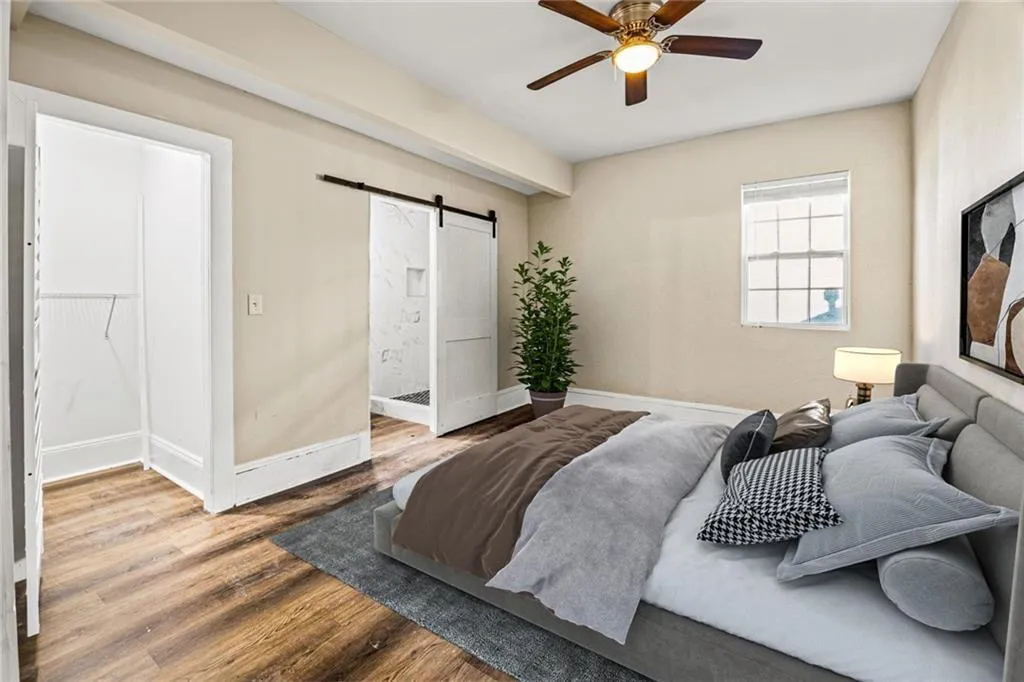 Bedroom with a barn door, wood finished floors, ensuite bathroom, and ceiling fan