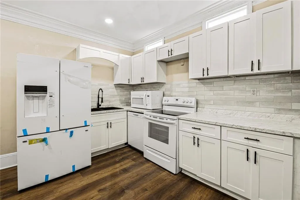Kitchen with white appliances, dark wood-type flooring, white cabinets, crown molding, and decorative backsplash