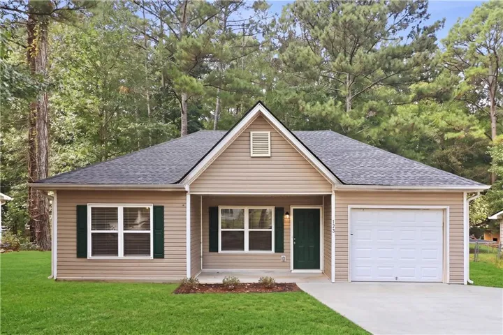 Single-story residence featuring light brown siding, a dark gray shingled roof, a dark green entry door, and an attached single-car garage