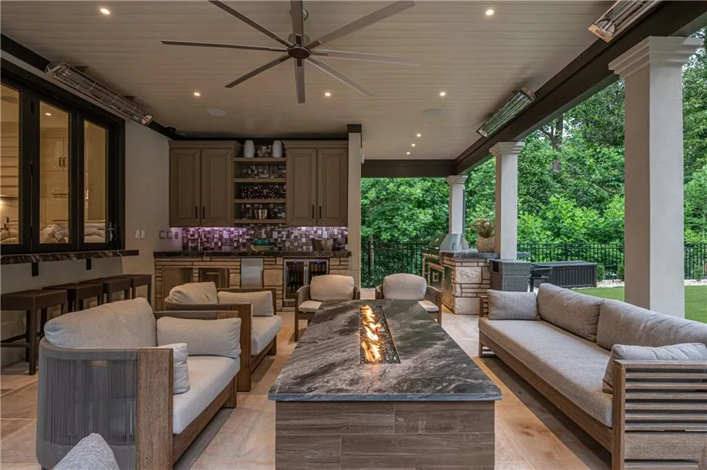 space featuring a built-in outdoor kitchen, patio heaters, ceiling fan, and linear fire table
