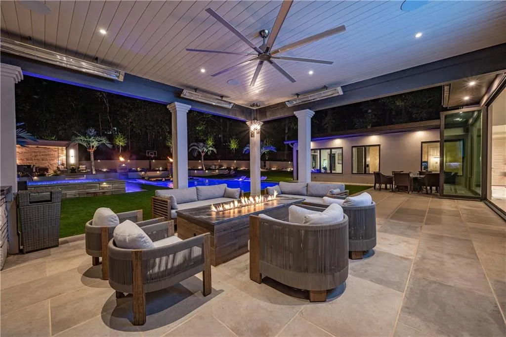 Covered outdoor living space featuring a built-in outdoor kitchen, patio heaters, ceiling fan, and linear fire table
