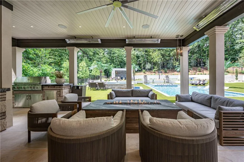 Covered outdoor living space featuring a built-in outdoor kitchen, patio heaters, ceiling fan, and linear fire table