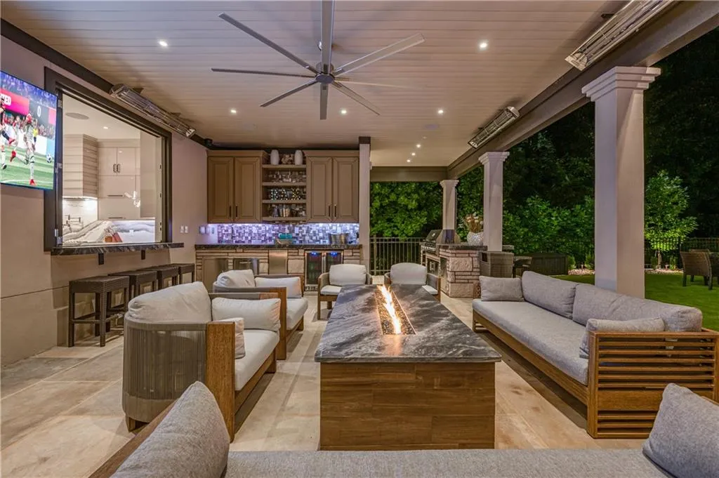 Covered outdoor living space featuring a built-in outdoor kitchen, patio heaters, ceiling fan, and linear fire table