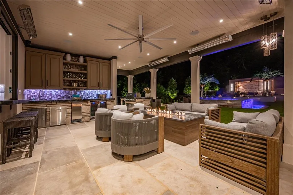 Covered outdoor living space featuring a built-in outdoor kitchen, patio heaters, ceiling fan, and linear fire table